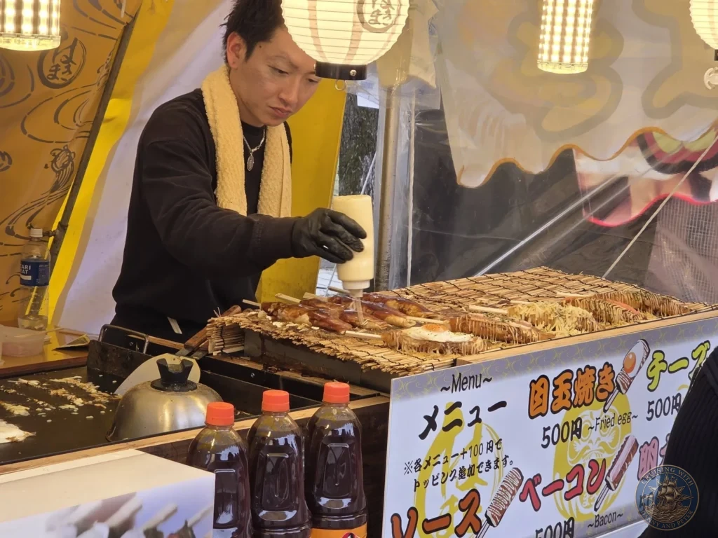 A Japanese festival vendor carefully squeezing mayonnaise onto freshly grilled skewers at a Yatai food stall set up during the cherry blossom festival at Matsue Castle during a shore excursion from Sakaiminato Japan Cruise Port Guide, DIY Sakaiminato Cruise Port to City Center, Things to do in Sakaiminato from cruise ship, Westerdam Sakaiminato Docking Location, One day in Sakaiminato Japan itinerary by Danny and Peter.