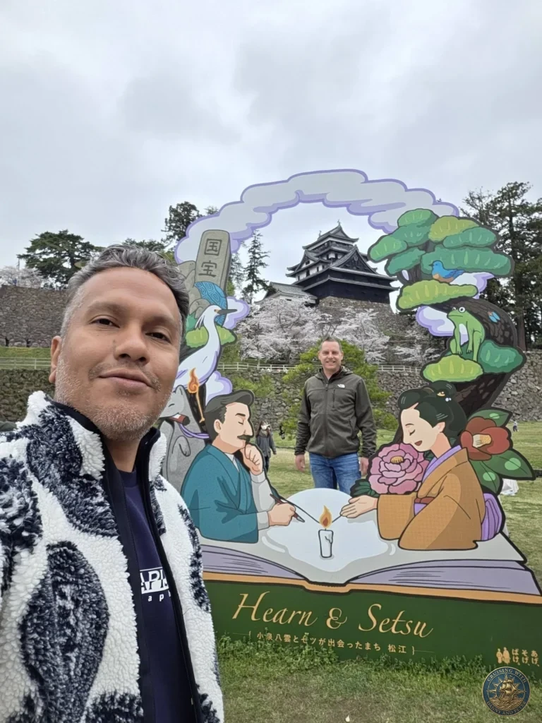 Danny taking a selfie with Peter standing inside a decorative Lafcadio Hearn and Setsu illustration frame with the black wooden keep of Matsue Castle rising in the background during a shore excursion from Sakaiminato Japan Cruise Port Guide, DIY Sakaiminato Cruise Port to City Center, Things to do in Sakaiminato from cruise ship, Westerdam Sakaiminato Docking Location, One day in Sakaiminato Japan itinerary by Danny and Peter.