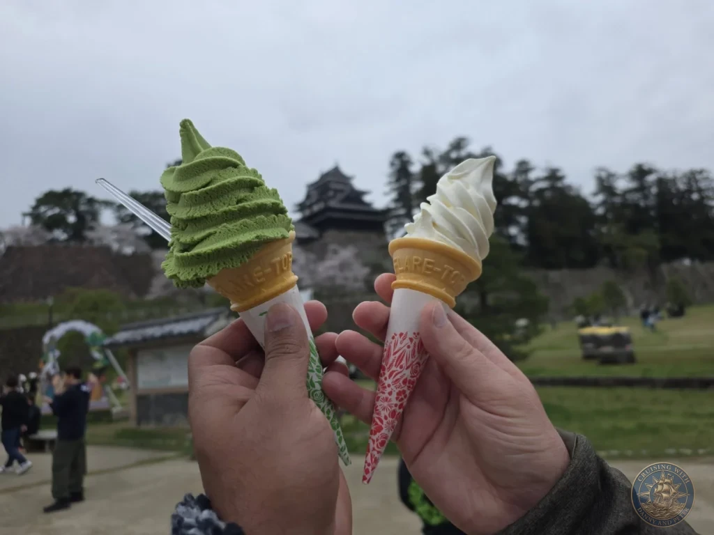 Danny and Peter holding green tea matcha and vanilla soft-serve ice cream cones in focus with the black keep of Matsue Castle soft-focused in the background during a shore excursion from Sakaiminato Japan Cruise Port Guide, DIY Sakaiminato Cruise Port to City Center, Things to do in Sakaiminato from cruise ship, Westerdam Sakaiminato Docking Location, One day in Sakaiminato Japan itinerary by Danny and Peter.