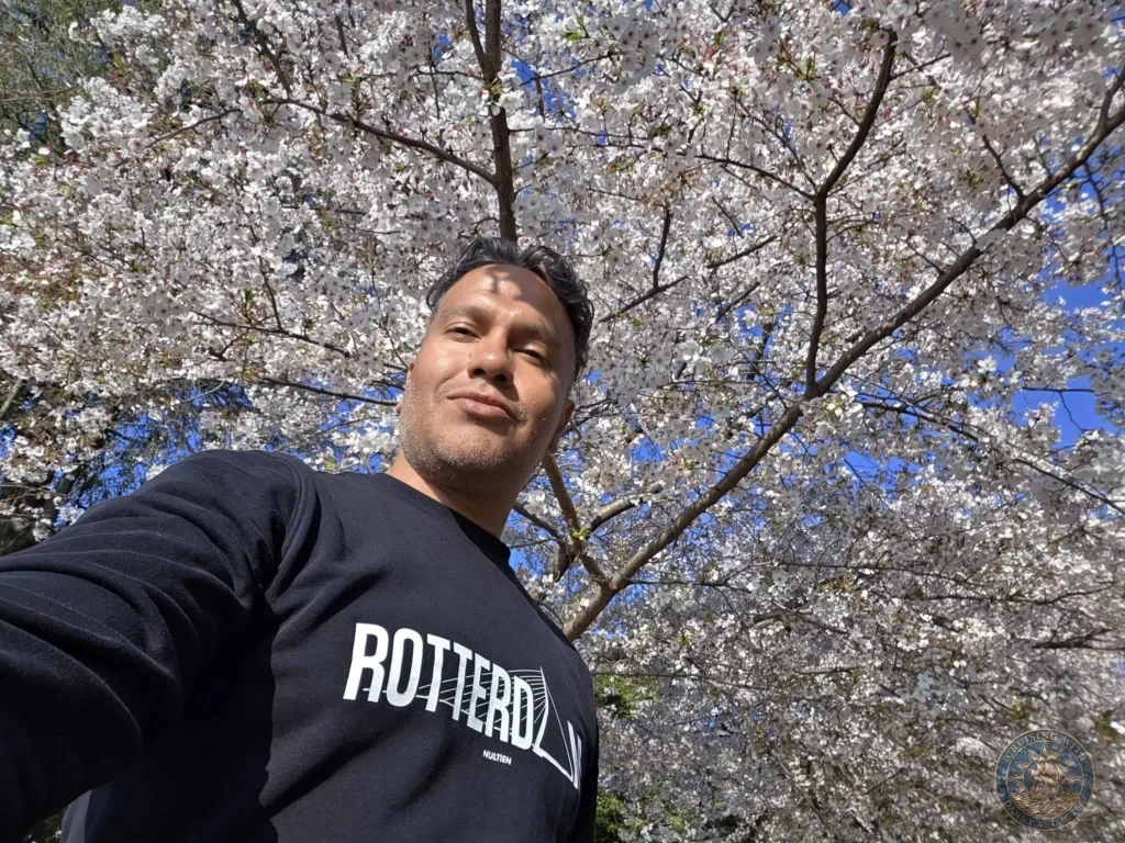 Hiroshima Japan Cruise Port Guide 2026 – Insider Tips & One Day Itinerary 70 A close-up selfie framed by a dense canopy of pink cherry blossoms in full bloom under a bright blue sky in Peace Memorial Park in Hiroshima Japan. Hiroshima Japan Cruise Port Guide, DIY Hiroshima Cruise Port to City Center, Things to do in Hiroshima from cruise ship, Westerdam Hiroshima Docking Location, One day in Hiroshima Japan itinerary by Danny and Peter.