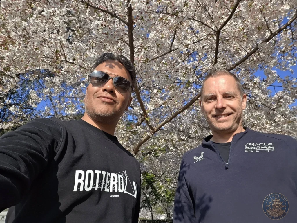 Hiroshima Japan Cruise Port Guide 2026 – Insider Tips & One Day Itinerary 72 A smiling selfie of Danny and Peter standing beneath a vibrant canopy of pale pink cherry blossoms blooming under a clear blue sky in Peace Memorial Park in Hiroshima Japan. Hiroshima Japan Cruise Port Guide, DIY Hiroshima Cruise Port to City Center, Things to do in Hiroshima from cruise ship, Westerdam Hiroshima Docking Location, One day in Hiroshima Japan itinerary by Danny and Peter.