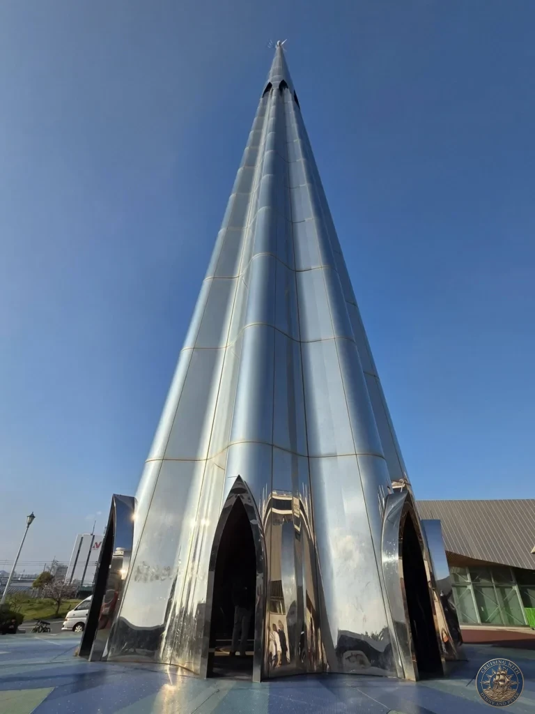 Hiroshima Japan Cruise Port Guide 2026 – Insider Tips & One Day Itinerary 29 A towering metallic spire structure reflecting sunlight against a clear blue sky at Miyajimaguchi Ferry Terminal near Hiroshima Japan. Hiroshima Japan Cruise Port Guide, DIY Hiroshima Cruise Port to City Center, Things to do in Hiroshima from cruise ship, Westerdam Hiroshima Docking Location, One day in Hiroshima Japan itinerary by Danny and Peter.
