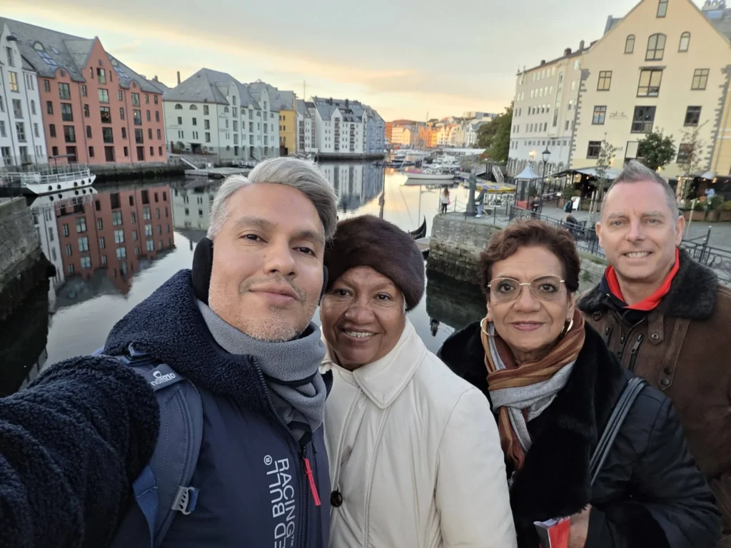 Group selfie along the scenic Brosundet canal with Art Nouveau architecture and serene water reflections in the background. Ålesund Norway Cruise Port Guide, DIY Ålesund Cruise Port to City Center, Things to do in Ålesund from cruise ship, Rotterdam Ålesund Docking Location, One day in Ålesund Norway itinerary, by Danny and Peter.