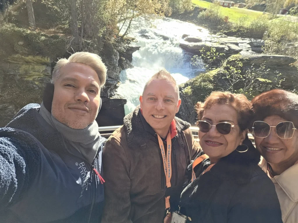 Danny taking a group selfie with Peter and family at the Gudbrandsjuvet Gorge viewing platform with rushing river rapids behind them during a Holland America Rotterdam shore excursion stop. Things to do in Ålesund from cruise ship, by Danny and Peter.