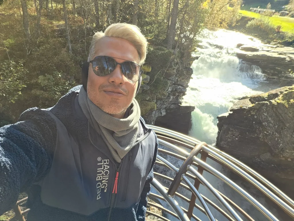 Danny taking a solo selfie wearing sunglasses on the viewing platform at Gudbrandsjuvet Gorge with rushing river waterfalls behind him during a Holland America Rotterdam excursion. Things to do in Ålesund from cruise ship, by Danny and Peter.