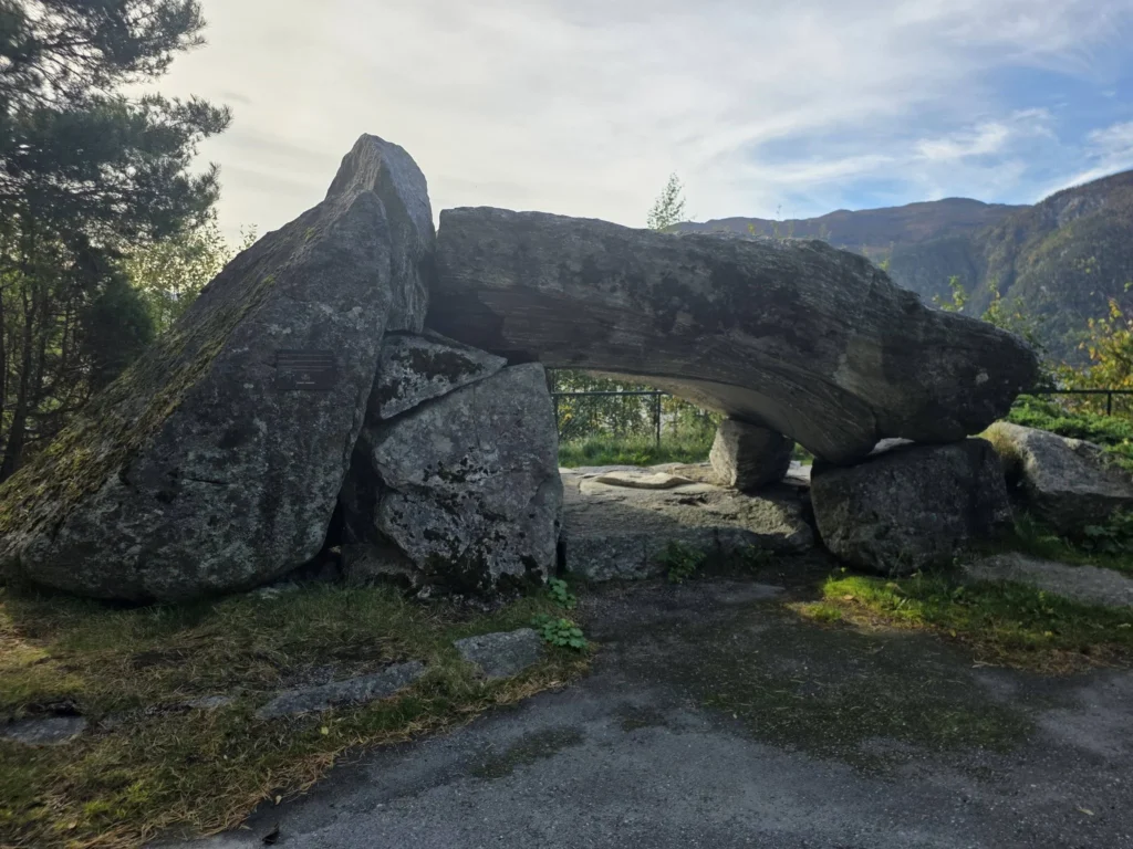 Large stone arch rock formation monument at Kokarsteinen Viewpoint with mountains in the background during a Holland America Rotterdam shore excursion. Things to do in Ålesund from cruise ship, by Danny and Peter.