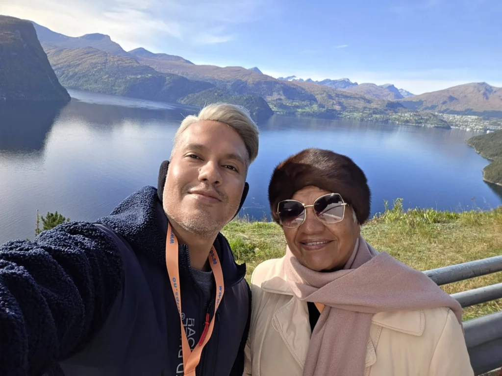 Danny taking a selfie with his mother at the Kokarsteinen Viewpoint overlooking the blue fjord and surrounding mountains during a Holland America Rotterdam shore excursion. Things to do in Ålesund from cruise ship, by Danny and Peter.