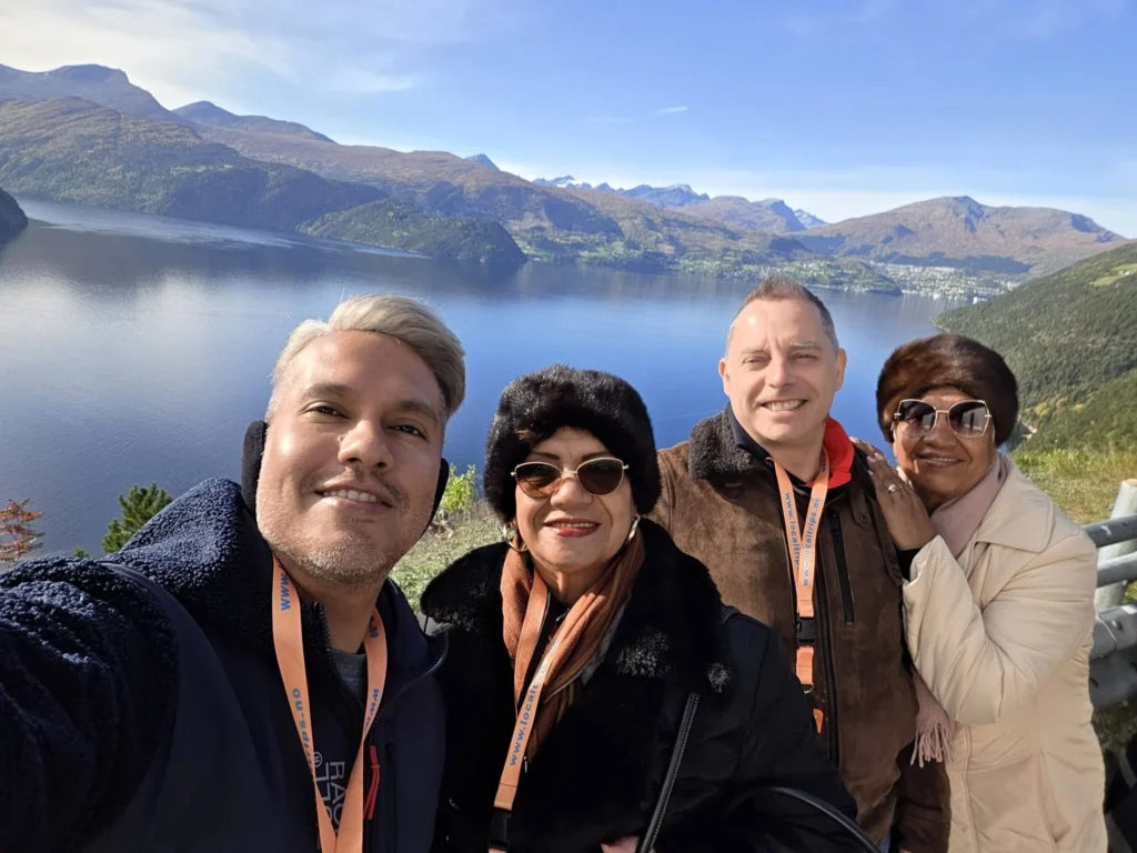 Danny taking a group selfie with Peter and family overlooking the panoramic fjord and mountain scenery at Kokarsteinen Viewpoint during a Holland America Rotterdam shore excursion. Things to do in Ålesund from cruise ship, by Danny and Peter.