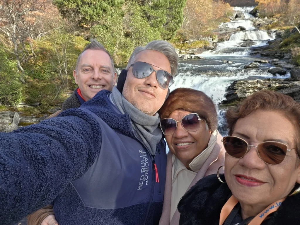 Danny taking a group selfie with Peter, his mother, and his aunt in front of the cascading stream at Krikebrua Waterfall Bridge during a Holland America Rotterdam shore excursion. Things to do in Ålesund from cruise ship, by Danny and Peter.