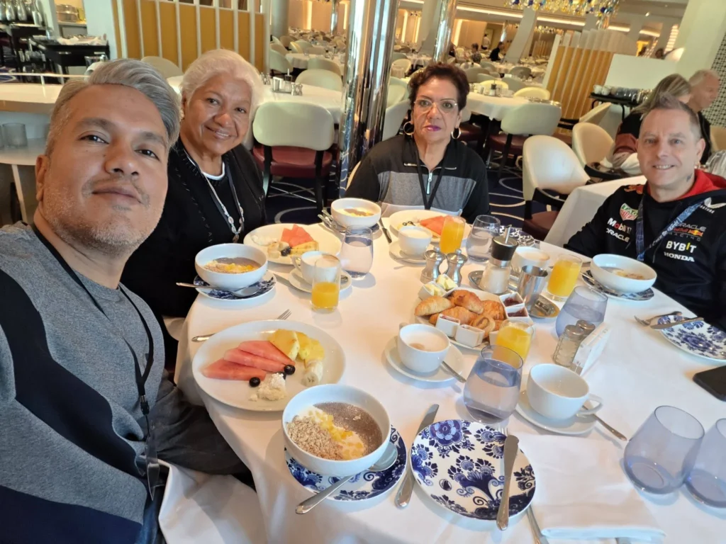 A group selfie showing a table filled with fresh fruit, pastries, juice, and yogurt bowls inside the main dining room onboard Holland America Line's ship Rotterdam during a visit to Ålesund. Things to do in Ålesund from cruise ship, by Danny and Peter.