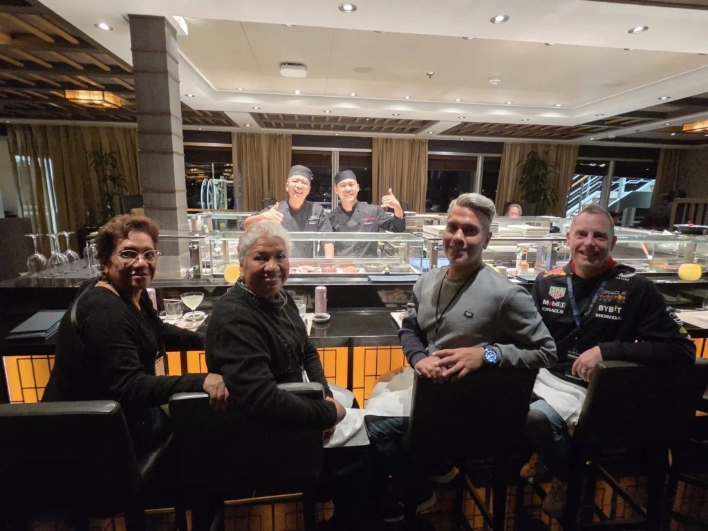 Danny, Peter, Danny's mother, and his aunt seated at the sushi counter with chefs smiling in the background inside Morimoto by Sea onboard Holland America Line's ship Rotterdam during a cruise to Ålesund. Things to do in Ålesund from cruise ship, by Danny and Peter.