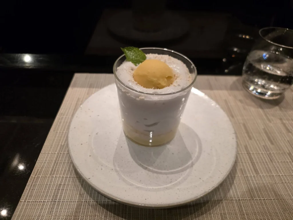 An elegantly layered dessert in a glass topped with sorbet and a fresh mint leaf, served on a white ceramic plate inside Morimoto by Sea onboard Holland America Line's ship Rotterdam during a cruise to Ålesund. Things to do in Ålesund from cruise ship, by Danny and Peter.