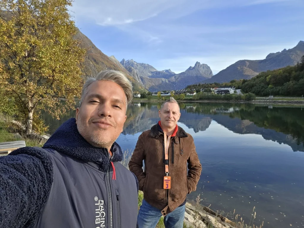 Danny taking a selfie with Peter standing by a calm lake reflecting rugged mountain peaks and golden autumn trees near Ålesund during a Holland America Rotterdam shore excursion. Things to do in Ålesund from cruise ship, by Danny and Peter.