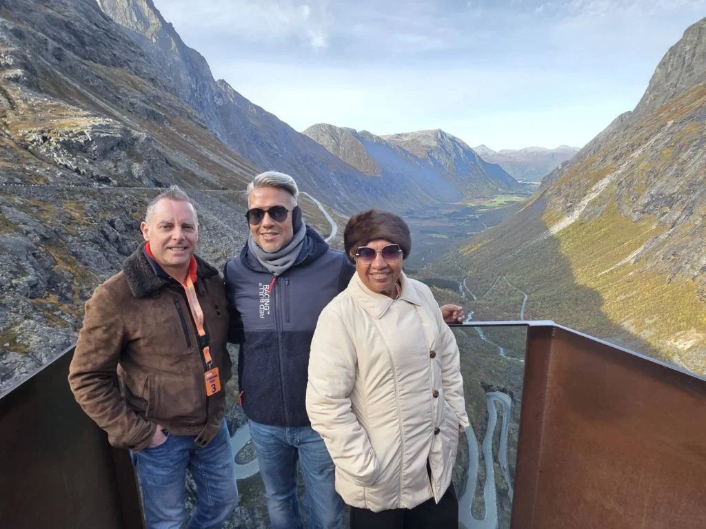 Peter, Danny, and Danny's mother posing together on the edge of the Trollstigen viewing platform overlooking the valley and mountains near Ålesund, Norway. Things to do in Ålesund from cruise ship, by Danny and Peter.