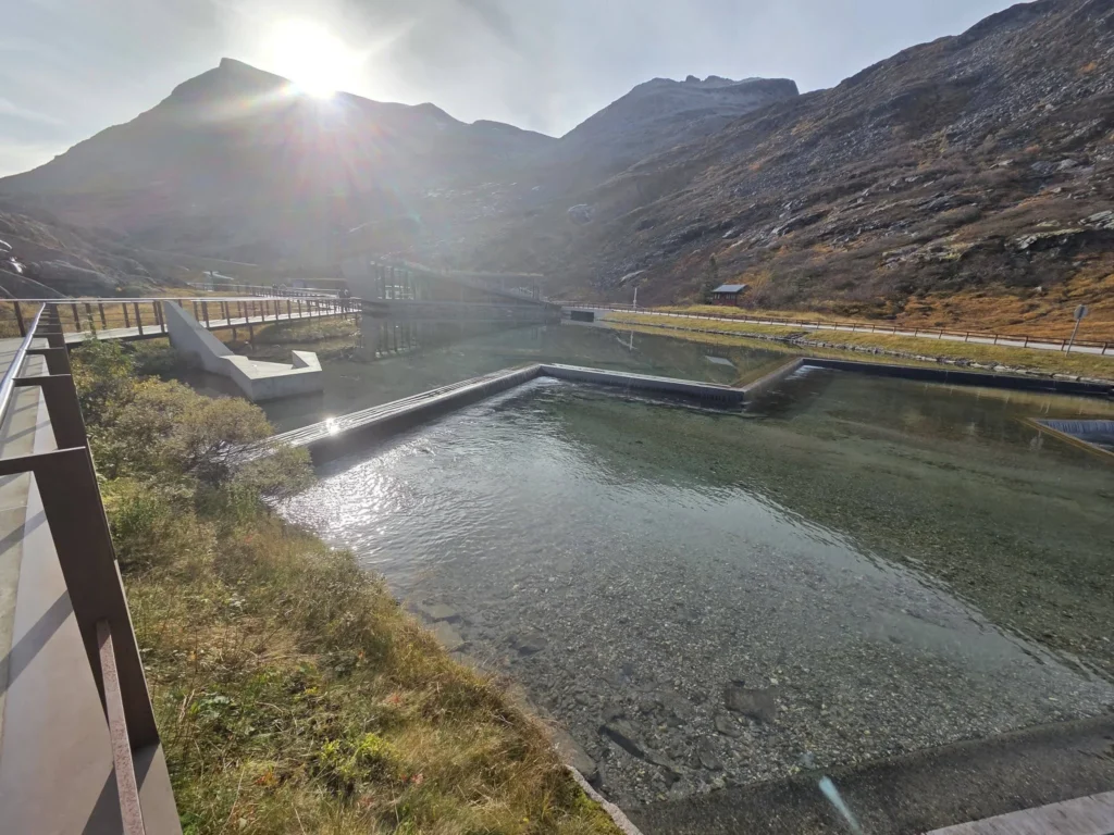 Bright sunlight shining over mountain peaks above the architectural reflecting pool and modern visitor center building at the Trollstigen plateau near Ålesund, Norway. Things to do in Ålesund from cruise ship, by Danny and Peter.